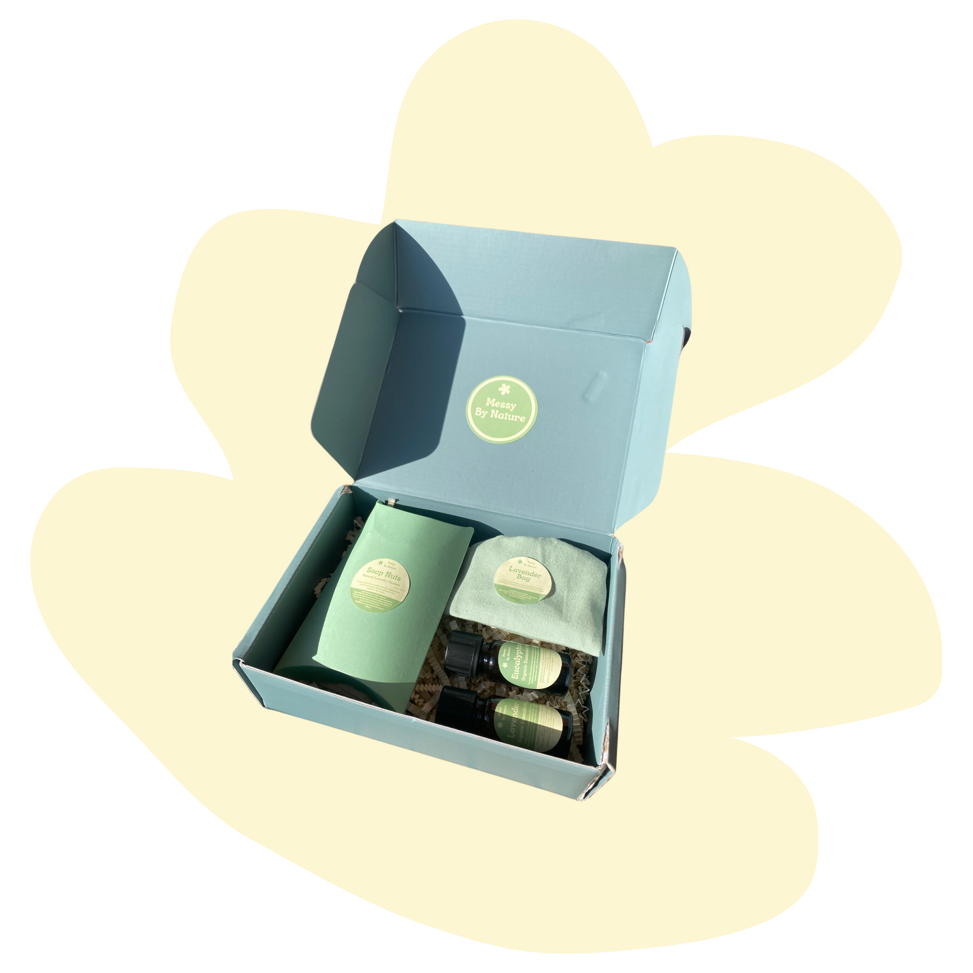 Image of a blue gift set with cream background in a squiggly shape. The gift set contains a blue box which says soap berries on the label, 2 essential oils with green labels and a lavender bag.